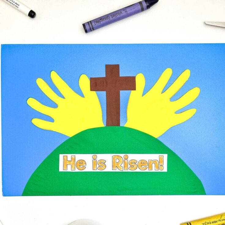 Colorful Easter-themed craft with yellow handprints, a brown paper cross, and a vibrant green hill on a blue background, featuring the message "He is Risen!" for celebrating Easter.