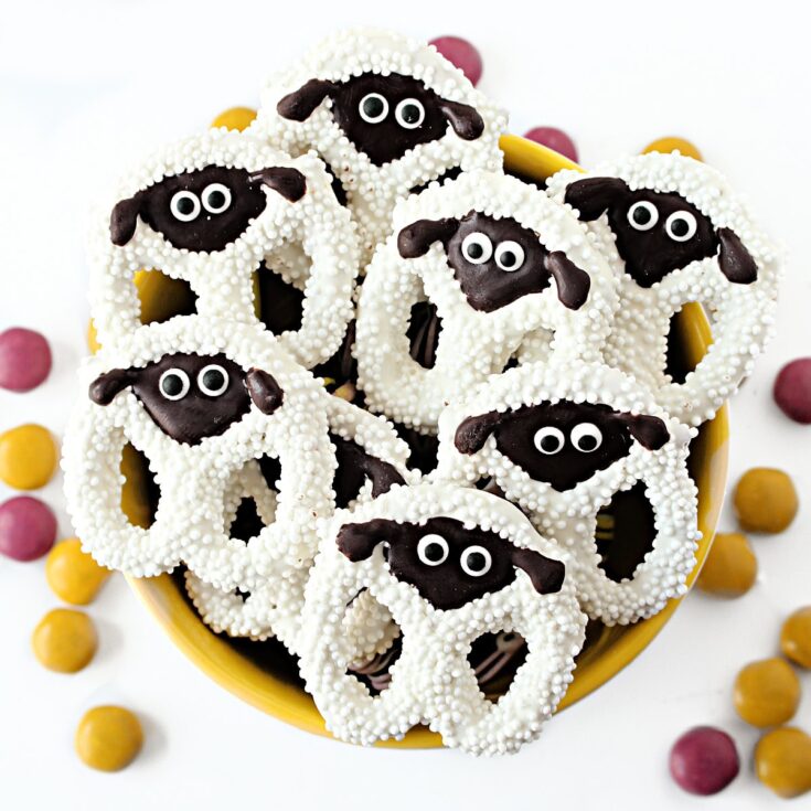 Cute sheep-shaped sugar cookies decorated with black and white icing, edible eyes, and sprinkles, perfect for baked goods and dessert displays.