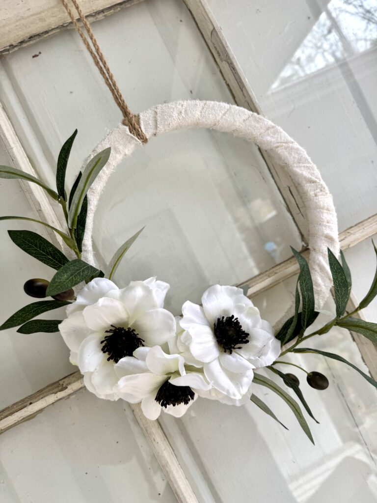 Elegant floral DIY wreath featuring white flowers and greenery, perfect for home decor or special occasions, crafted with a rustic jute hanger and soft fabric details.