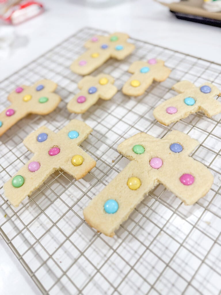 Colorful cross-shaped sugar cookies decorated with pastel sprinkles, cooling on a wire rack ready for decorating or serving. Perfect for Easter, spring celebrations, or special occasions with a sweet touch.