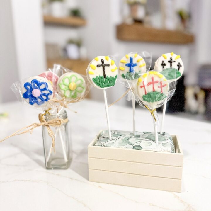 Colorful religious-themed decorated cookies on sticks, suitable for Christian celebrations, displayed on a white surface with a modern kitchen background.