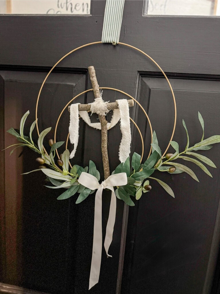 Rustic cross wall decor with olive branch wreath, white ribbon accent, and hanging wood elements, perfect for farmhouse or boho holiday home Christmas wreath decorations.