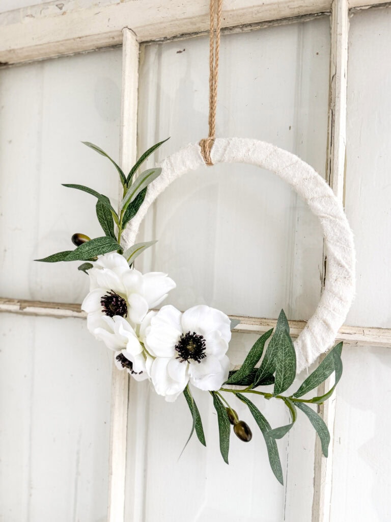 Soft white floral wreath with greenery on cream wall, ideal for shabby chic or rustic home decor, handcrafted flower wreath, perfect for farmhouse aesthetic, lifestyle decor or wedding accessories.