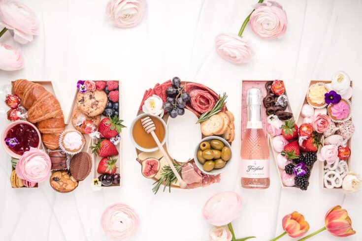 Delicious breakfast spread with assorted pastries, fruits, and beverages arranged to spell out "LOVE" with pink flowers and elegant presentation.