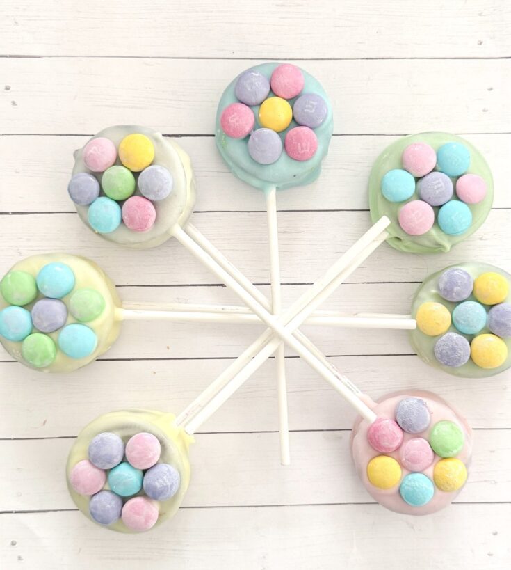 Colorful pastel candy lollipops decorated with mini M&M chocolates on white wooden background, perfect for sweet treats, party favors, and dessert table displays.