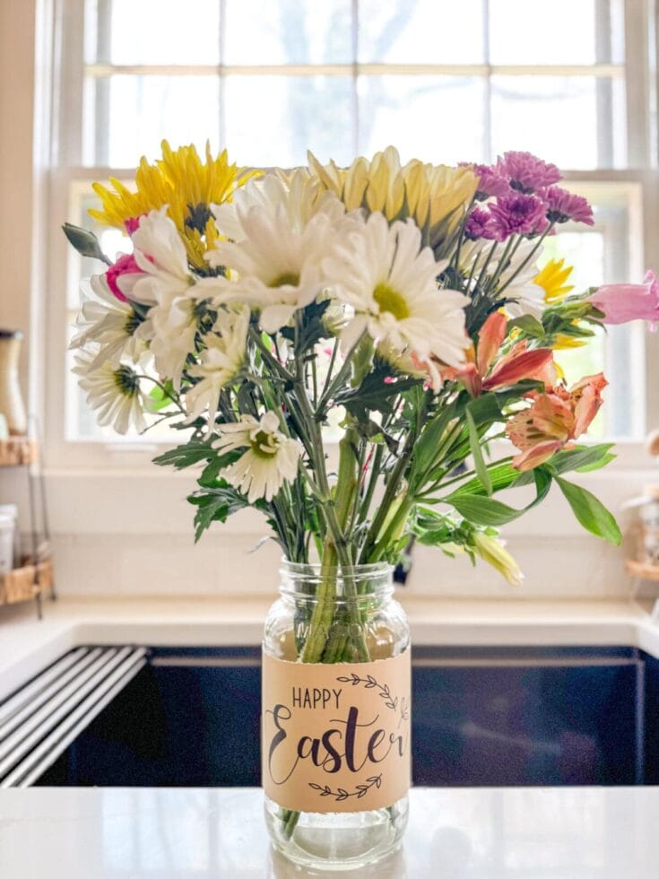 Vase with fresh spring flowers including daisies, lilies, and chrysanthemums on a countertop with an "Happy Easter" label, symbolizing celebration, spring, and holiday greetings.
