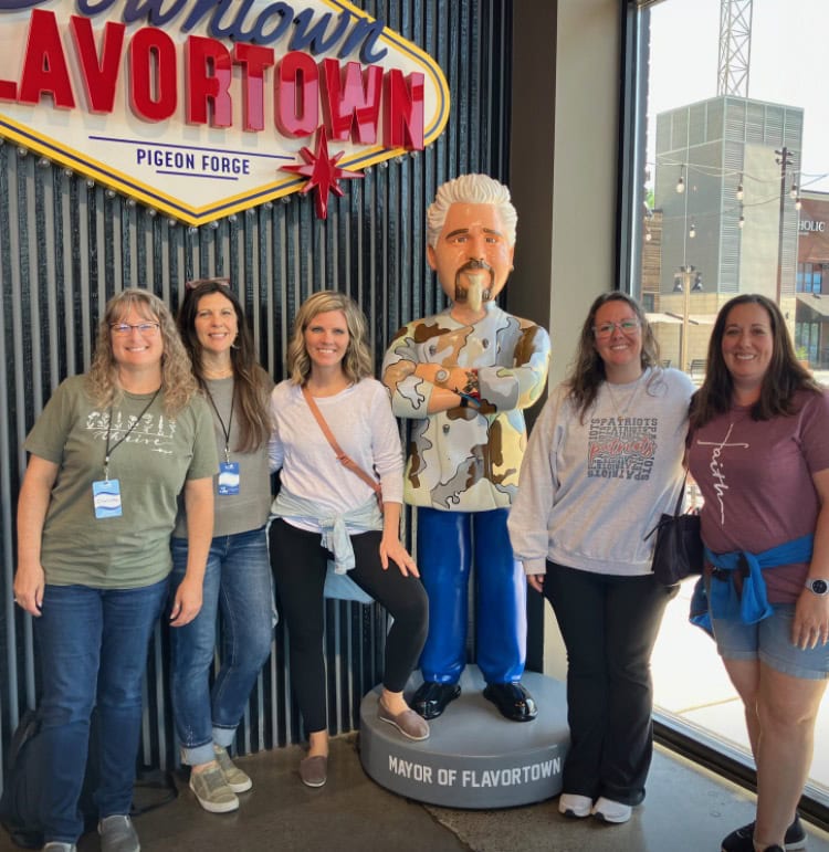 Flavortown mayor sculpture with group of smiling women in tourist attire at Pigeon Forge, Tennessee, celebrating local flavor and food culture.