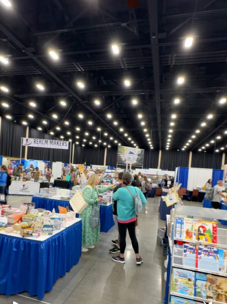 Bright indoor bookstore at the A Hundred Affections event, showcasing tables filled with books and attendees browsing and engaging with vendors.