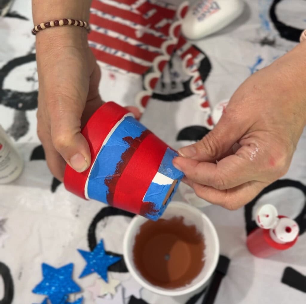 Spray paint being applied to a cylindrical object in an art craft project with blue and red colors.