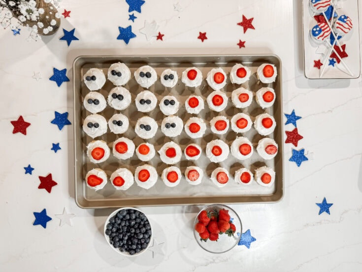 Patriotic-themed mini cupcakes with strawberries and blueberries, surrounded by red, white, and blue star-shaped decorations for a festive celebration.