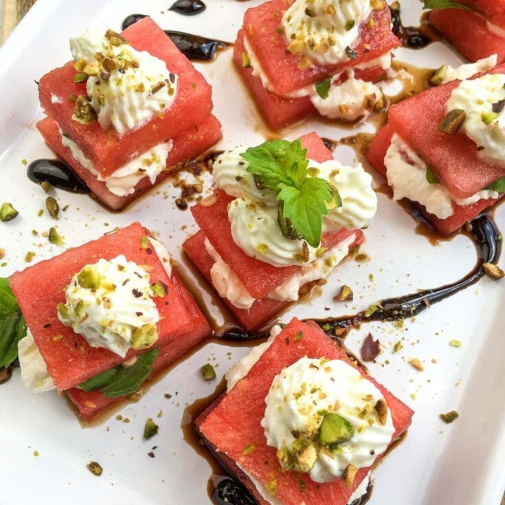 Sweet watermelon dessert bites topped with whipped cream, chopped pistachios, and a drizzle of chocolate sauce, garnished with fresh mint leaves for a delicious and refreshing treat.