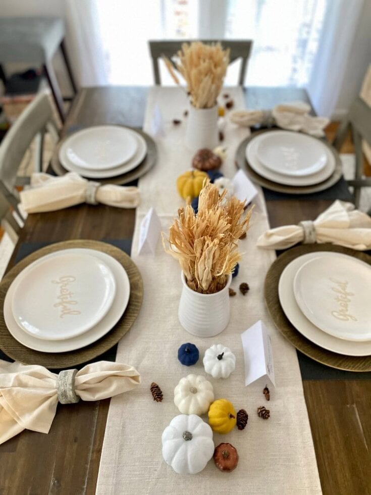 Autumn-themed dining table setup with neutral-toned table runner, white pumpkin decorations, dried pampas grass centerpieces, and elegant place settings for a cozy, stylish fall celebration.