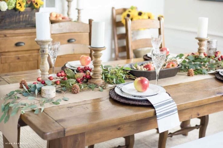 A festive dining table decorated with candles, apples, greenery, and pinecones, perfect for an autumn or holiday celebration at A Hundred Affections.