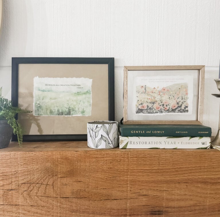 Soft watercolor art prints with uplifting biblical quotes, displayed on a wooden surface with decorative items, creating a calming and spiritually inspiring home decor setup.