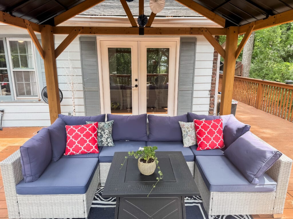 Red pillows on blue sectional under gazaebo on deck