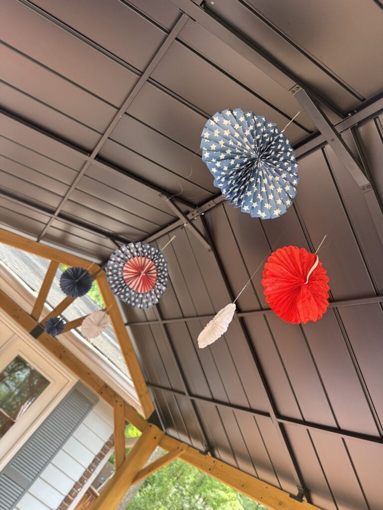 paper pinwheel rosettes hanging from top of gazebo for 4th of July decor 