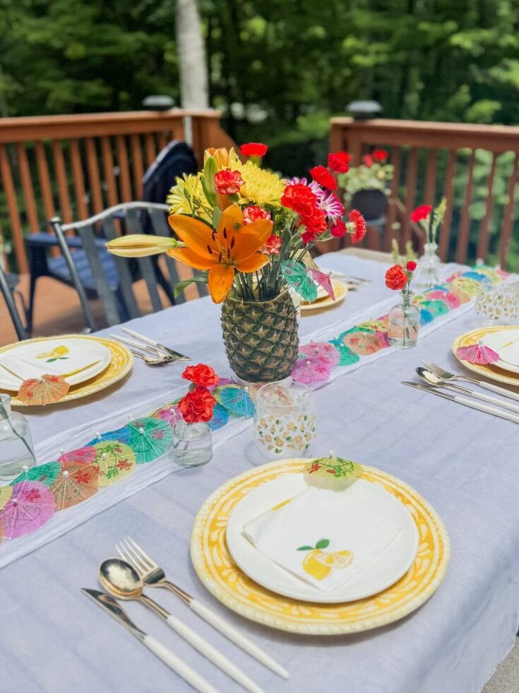 Colorful flower centerpiece on a summer outdoor dining table with vibrant tableware and paper umbrella decorations, perfect for a summer celebration or garden party.