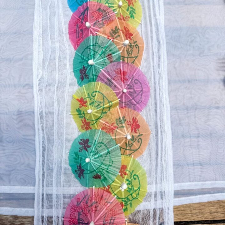 Colorful paper parasols with floral patterns arranged in a vertical line on a white textured fabric. Perfect for summer decor, outdoor events, and tropical-inspired design themes.