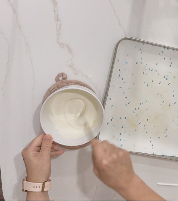 Cream being stirred in a bowl on a marble surface with a mirror beside it.