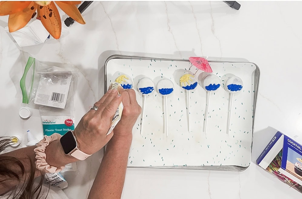 Colorful cake pops decorated with blue and yellow icing on a baking sheet.