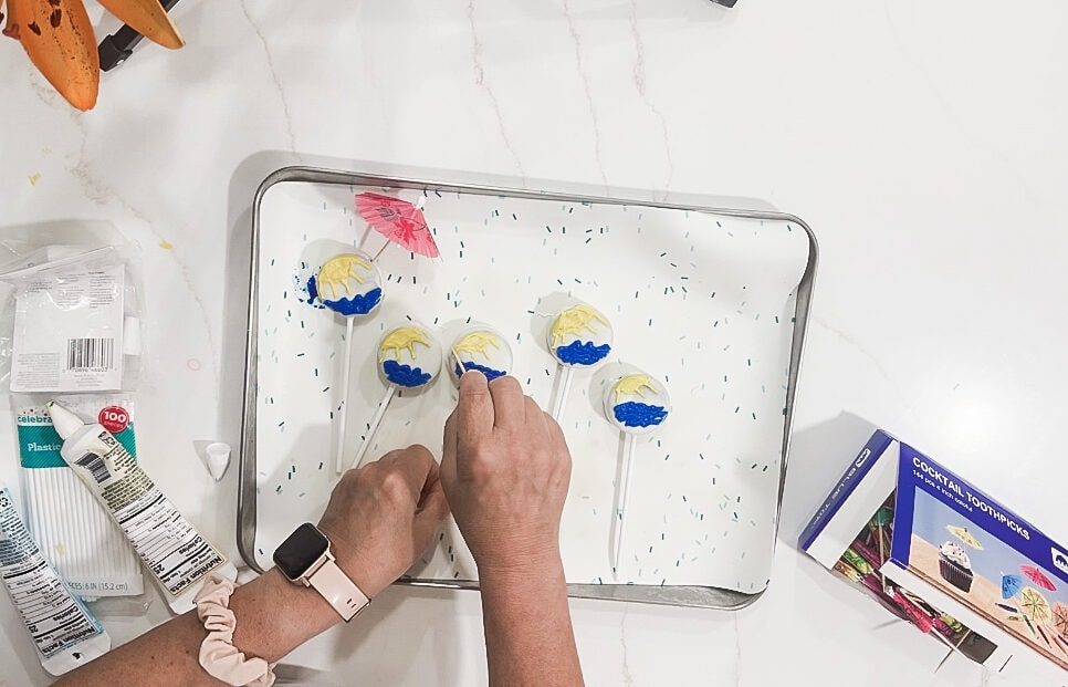 Colorful beach-themed cake pops with umbrellas on sticks, being decorated on a baking tray, perfect for summer parties and celebrations.