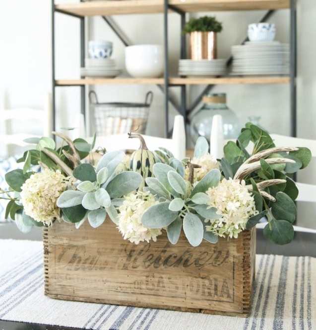 Rustic wooden crate centerpiece with eucalyptus, hydrangeas, and mini gourds for farmhouse home decor and floral arrangement ideas.