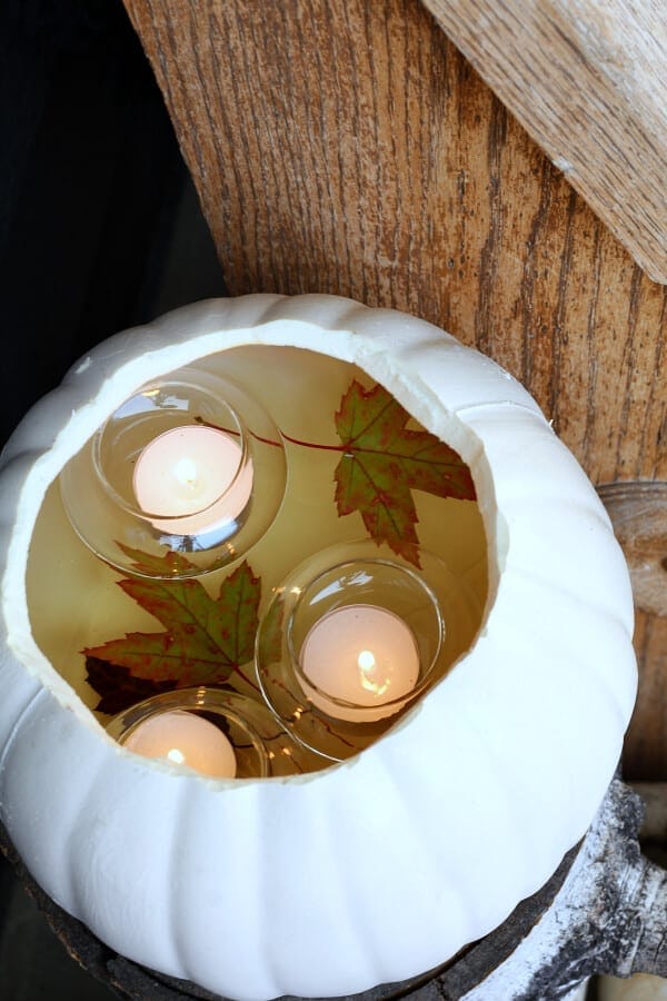 Thick white pumpkin-shaped candle holder with floating candles and autumn leaves, creating a cozy fall decor ambiance.
