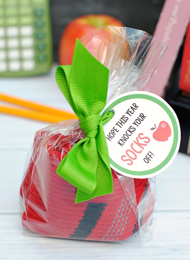 Bright red socks with gray accents, wrapped in clear cellophane with a vibrant green bow and a personalized holiday gift tag, perfect for gifting during the festive season.