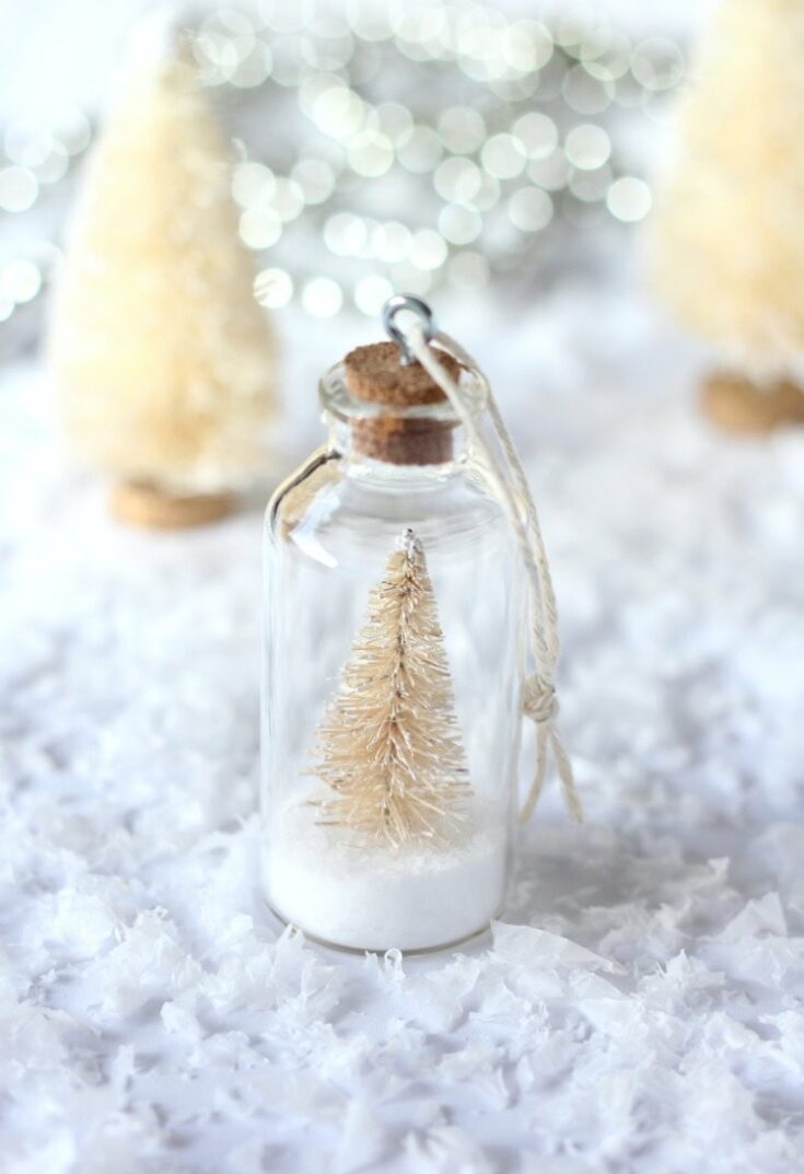Miniature beige Christmas tree inside a glass bottle with cork top, holiday winter decor, snowy scene, festive home decoration, Christmas craft, seasonal ornament, whimsical holiday theme.