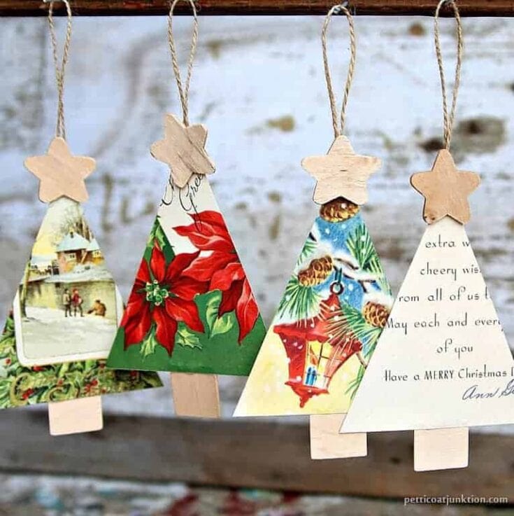 Photo of handmade Christmas tree-shaped ornaments with vintage holiday images and handwritten messages hanging on a rustic wood backdrop.