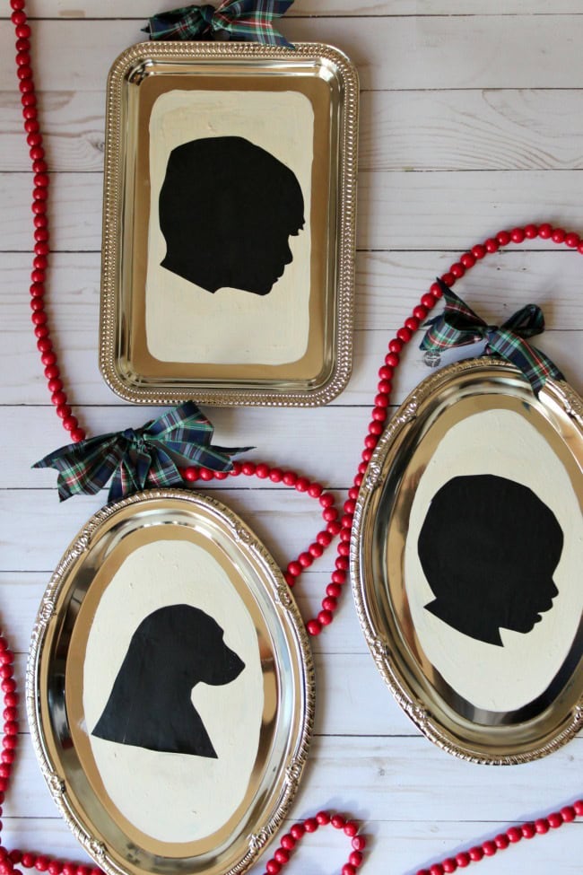Silhouette art featuring black profiles of a child's face and a dog's head on elegant silver trays, decorated with festive red beads and plaid bows, perfect for a custom pet or child-themed celebration.