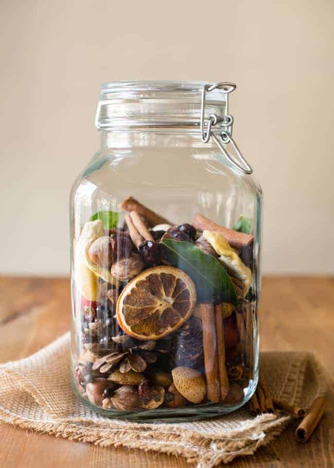 Dried herbs and citrus inside a glass jar, with cinnamon sticks and bay leaves, perfect for homemade potpourri or natural decor.