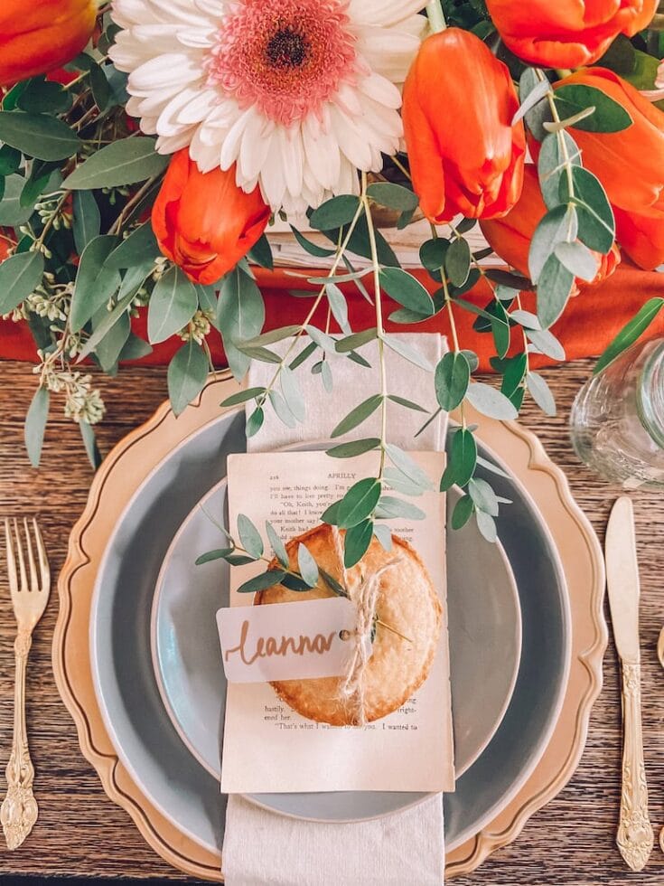 Vibrant floral centerpiece with white, pink, and orange flowers, greenery, and eucalyptus on a rustic wooden table with elegant tableware, perfect for a wedding or special celebration.