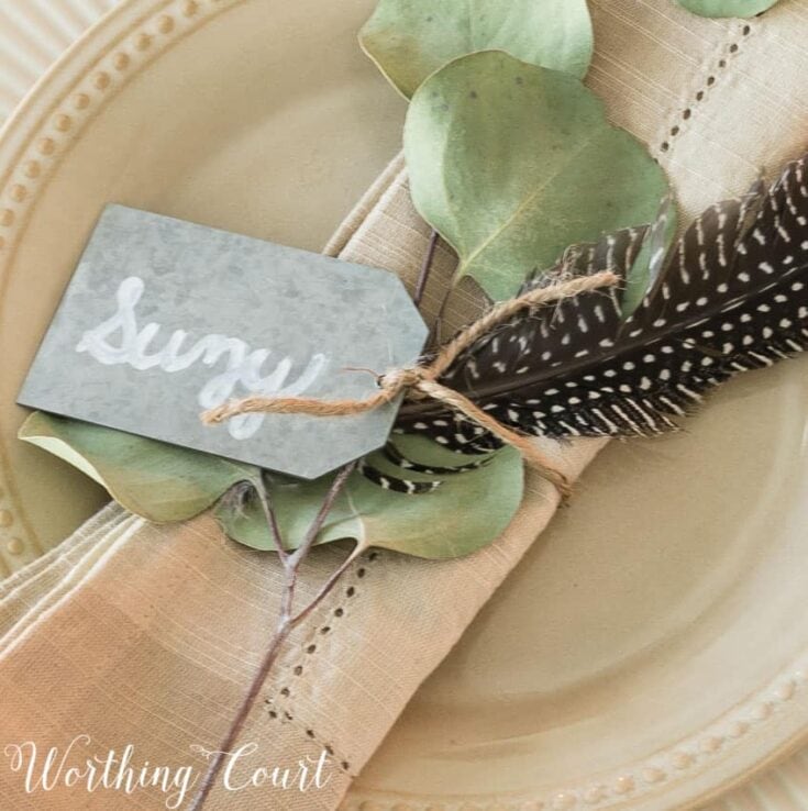 Dinner place setting with eucalyptus, feather, and handwritten napkin on elegant plate, perfect for rustic wedding or brunch, warm neutral tones.