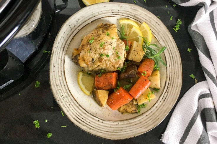 Creamy baked chicken leg with roasted carrots, potatoes, and herbs served with lemon wedges on a rustic plate. Perfect comfort food for a wholesome family dinner.