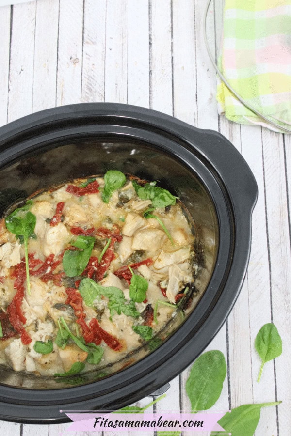 Creamy chicken and spinach stew cooked in a slow cooker with sun-dried tomatoes and fresh greens, served hot with a side of colorful striped napkin.