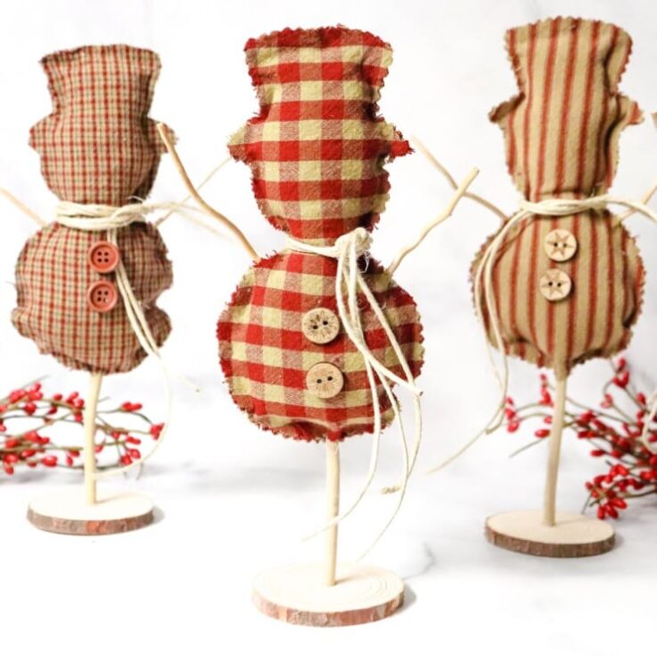 Red and beige checkered fabric snowman ornaments with button details, tied with twine, on wooden bases, perfect for holiday Christmas decor and rustic seasonal decoration, from A Hundred Affections.