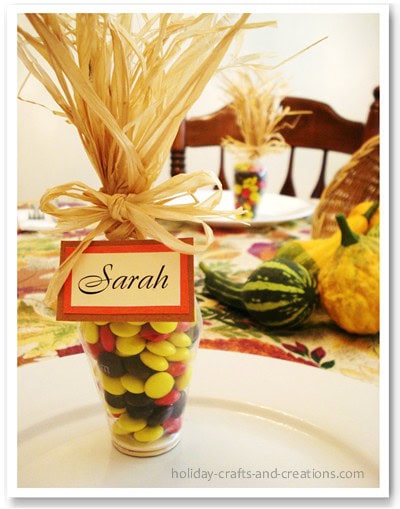 Colorful candy-filled glass jar as a personalized party favor with a "Sarah" name tag, decorated with natural raffia, perfect for festive celebrations.