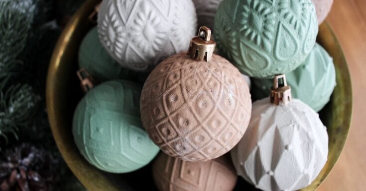 Soft pastel Christmas ornaments in a decorative bowl, featuring textured geometric and floral patterns for holiday decor and festive home decoration.