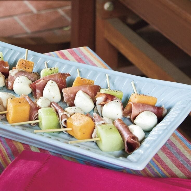Skewers with melon, mozzarella balls, prosciutto, and cherry tomatoes on a serving platter.