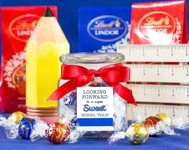 Sweet school year gift jar with Lindor chocolates, wrapped in a red ribbon, surrounded by colorful candy and Back to School supplies, perfect for celebrating teachers or students.