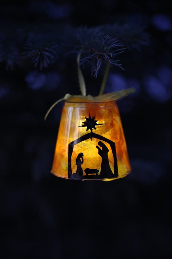 Handmade Christmas ornament with nativity scene silhouette in warm light, nestled among dark pine branches, creating a cozy holiday decoration.