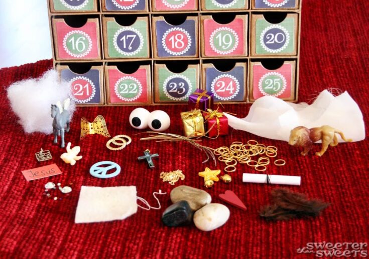Colorful advent calendar with numbered doors, surrounded by small festive and jewelry-themed toys, decorations, and figurines on a red textured surface.