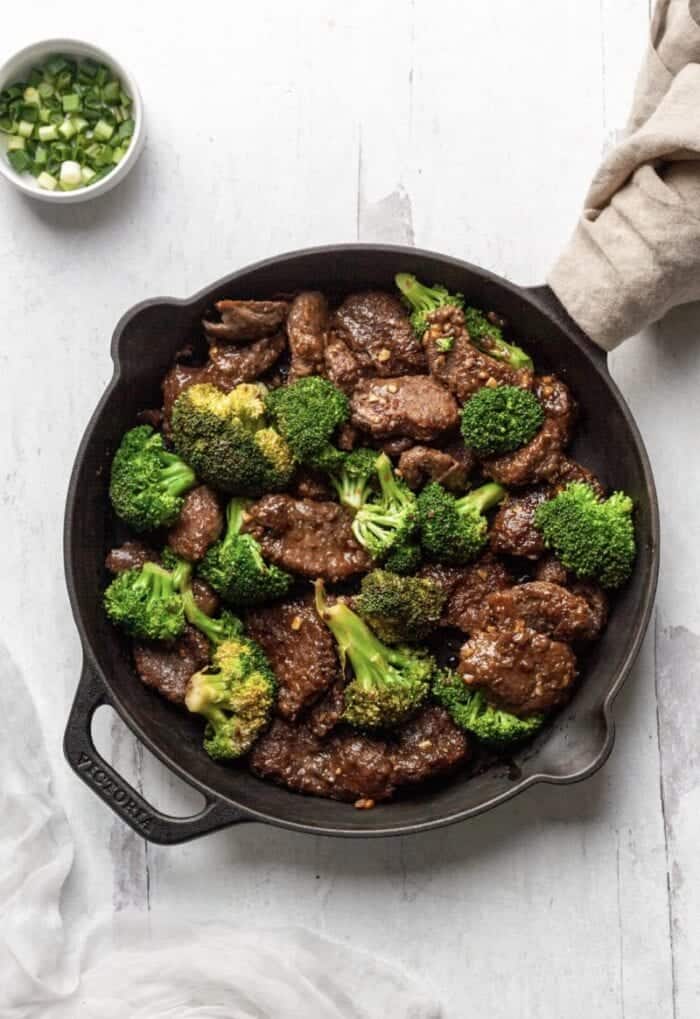 Savory beef and broccoli stir-fry in a cast iron skillet with chopped green onions on the side, healthy and flavorful Asian-inspired dish, perfect for quick weeknight dinners.