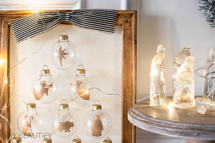 Delicate glass ornaments featuring holiday animals and stars, illuminated by warm fairy lights, displayed on a wooden frame for a cozy festive home decor.