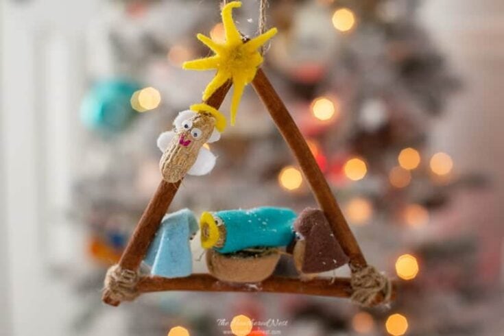Colorful handmade felt ornament featuring whimsical stars, characters, and designs, hanging as Christmas decor with blurred festive lights in the background.