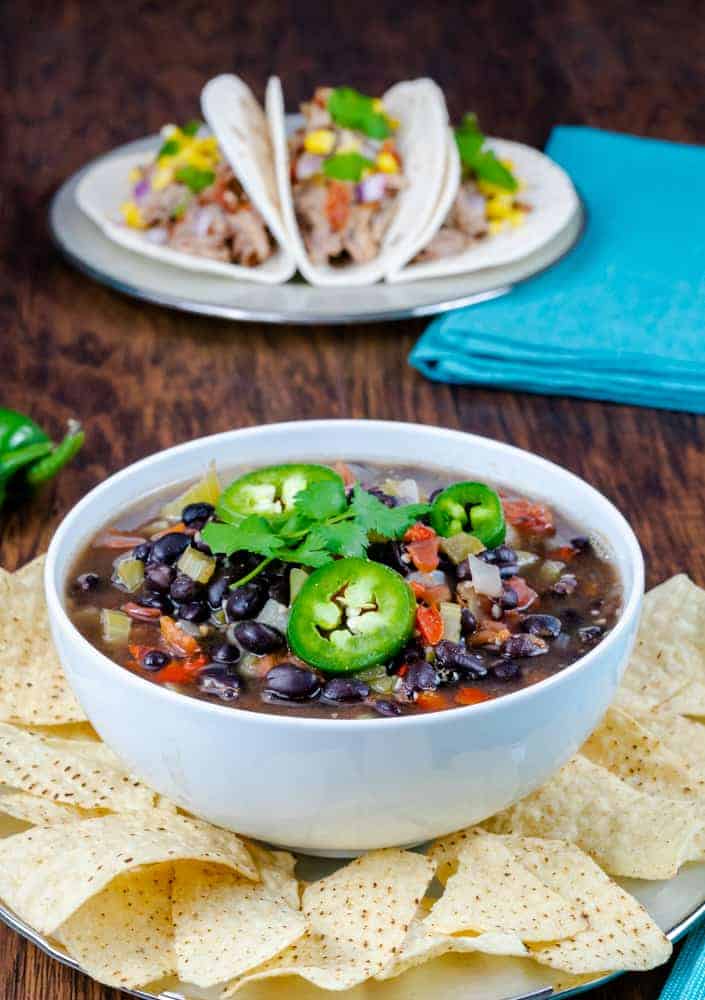 Creamy black bean soup topped with fresh jalapeño slices and cilantro, served with crispy tortilla chips on a rustic wooden table.