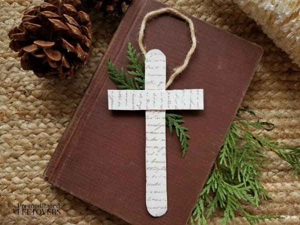 Handmade Christian cross ornament on a vintage Bible with pine tree accents and pine cone, ideal for holiday religious decor and spiritual gift ideas.