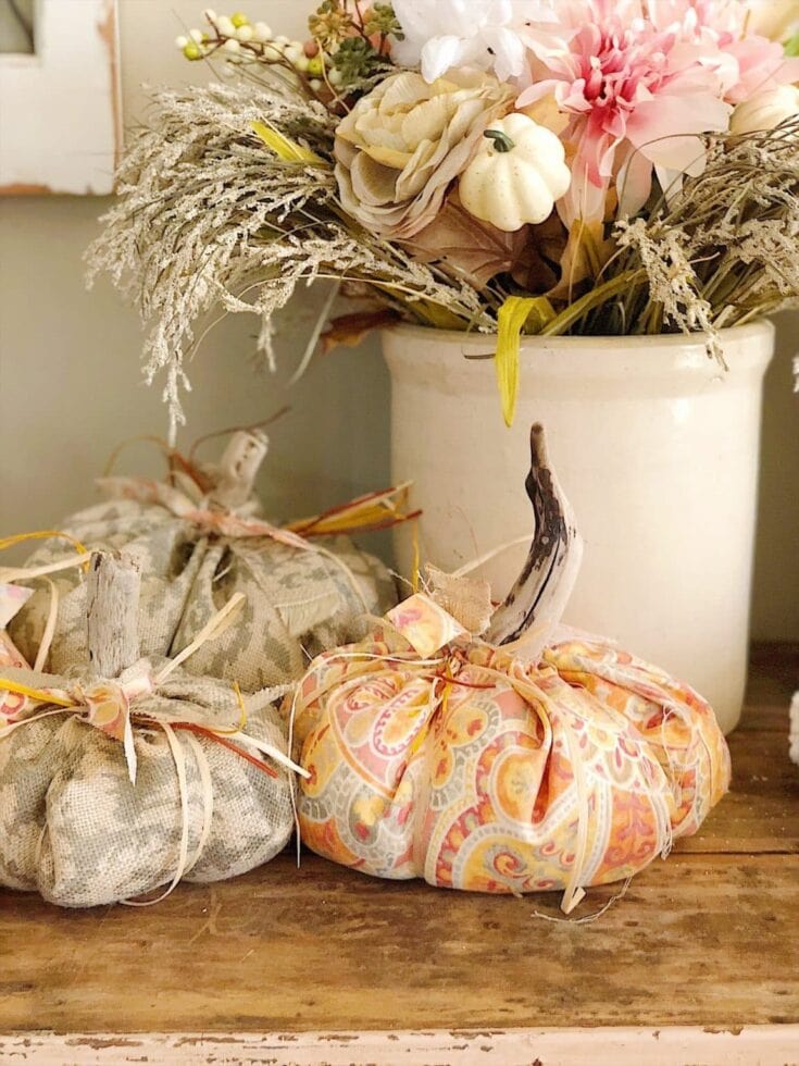 Vase with floral arrangement and decorative fabric pumpkins for fall, showcasing rustic autumn decor with dried flowers and seasonal accents.