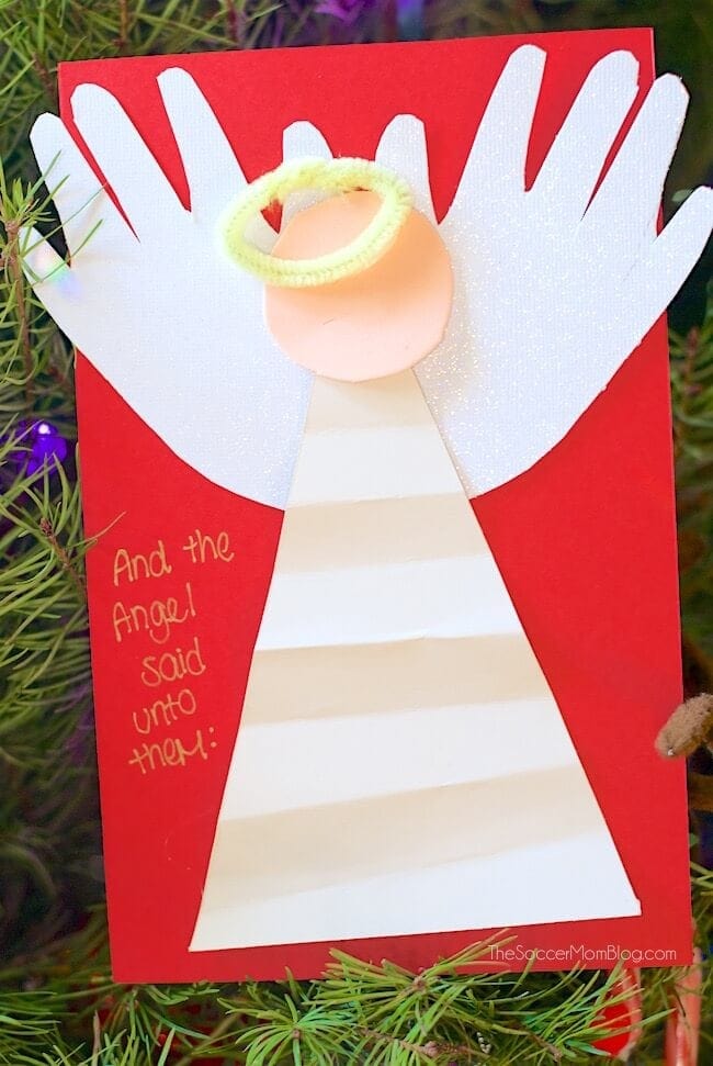 Angel nativity craft for Christmas, featuring a paper angel with a halo on a red background, surrounded by pine branches. Perfect for religious holiday celebrations and children's craft activities.